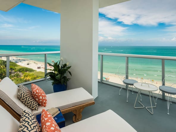 Balcón con vista al océano turquesa y la playa llena de vida, con muebles cómodos para relajarse.