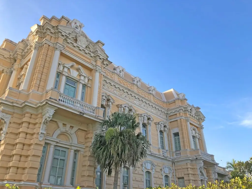 Fotografía del Palacio Cantón en Mérida, Yucatán, México. Edificio histórico de estilo neoclásico con fachada amarilla y detalles ornamentales blancos, bajo un cielo azul claro.